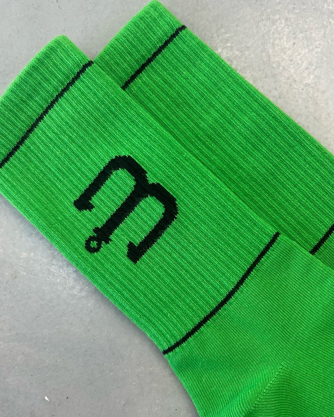 Bright green athletic socks with a black stylized 'm' logo and thin black horizontal stripes.