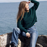 Cropped wool sweater in deep aqua green in front of ocean
