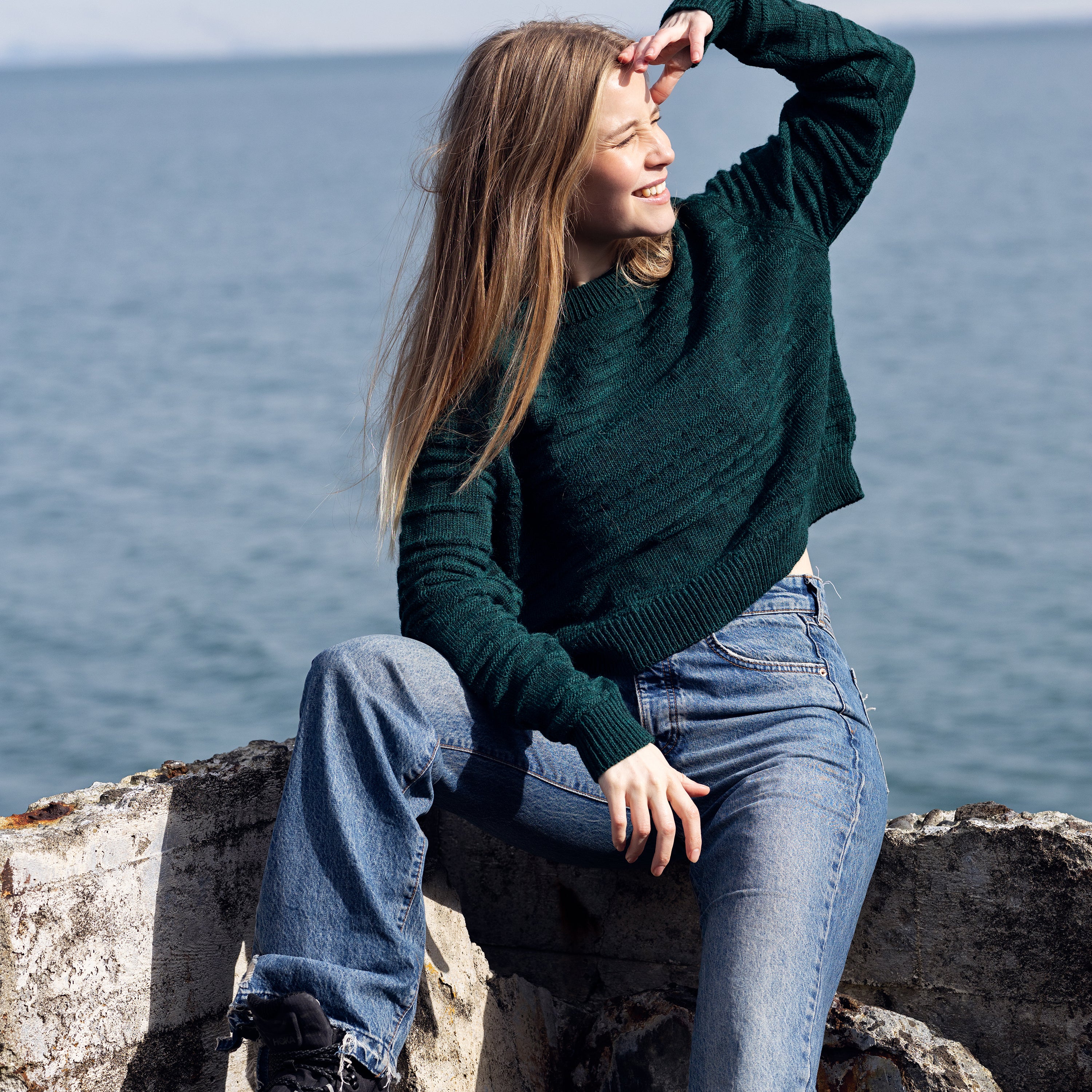 Cropped wool sweater in deep aqua green in front of ocean
